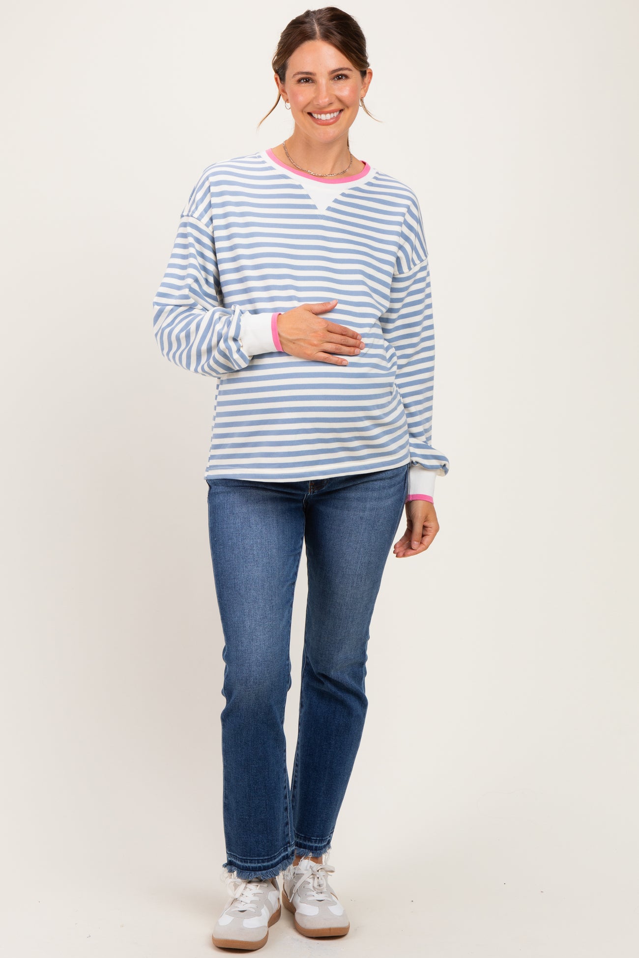 woman wearing a blue and white striped maternity sweatshirt with pink accents and holding her baby bump