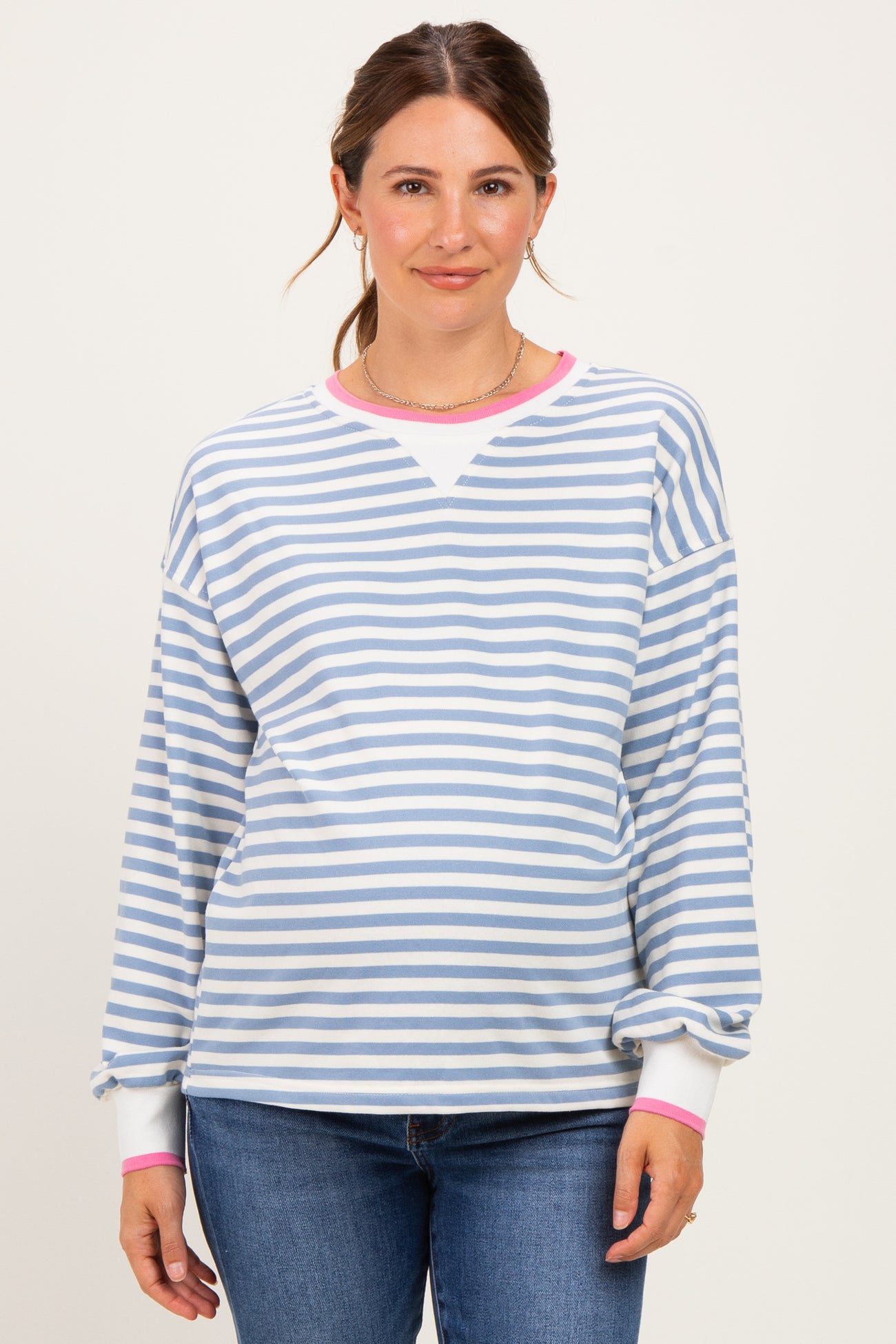 woman wearing a striped light blue and white maternity sweatshirt with pink cuffs and a visible baby bump