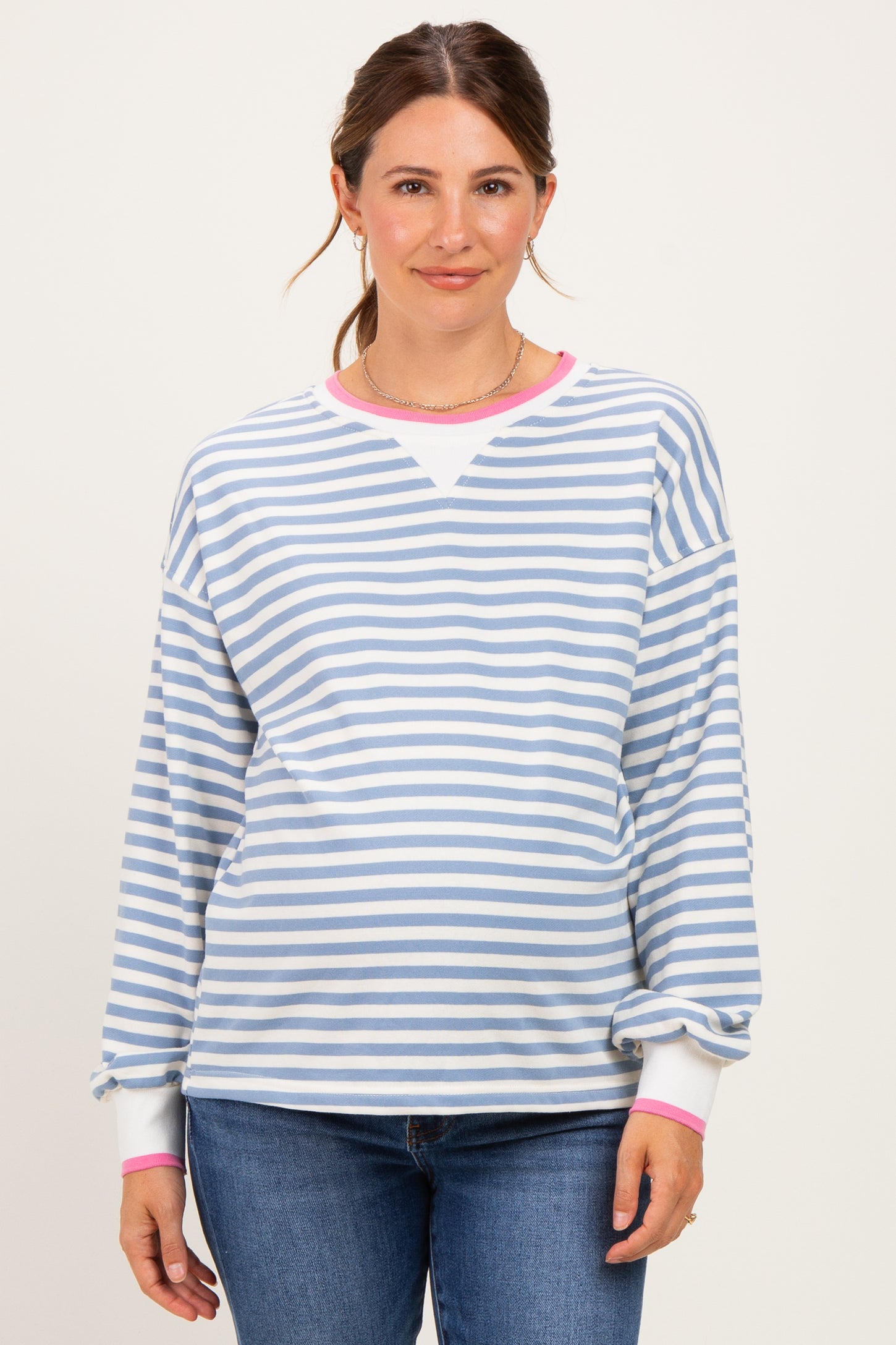 woman wearing a striped light blue and white maternity sweatshirt with pink cuffs and a visible baby bump