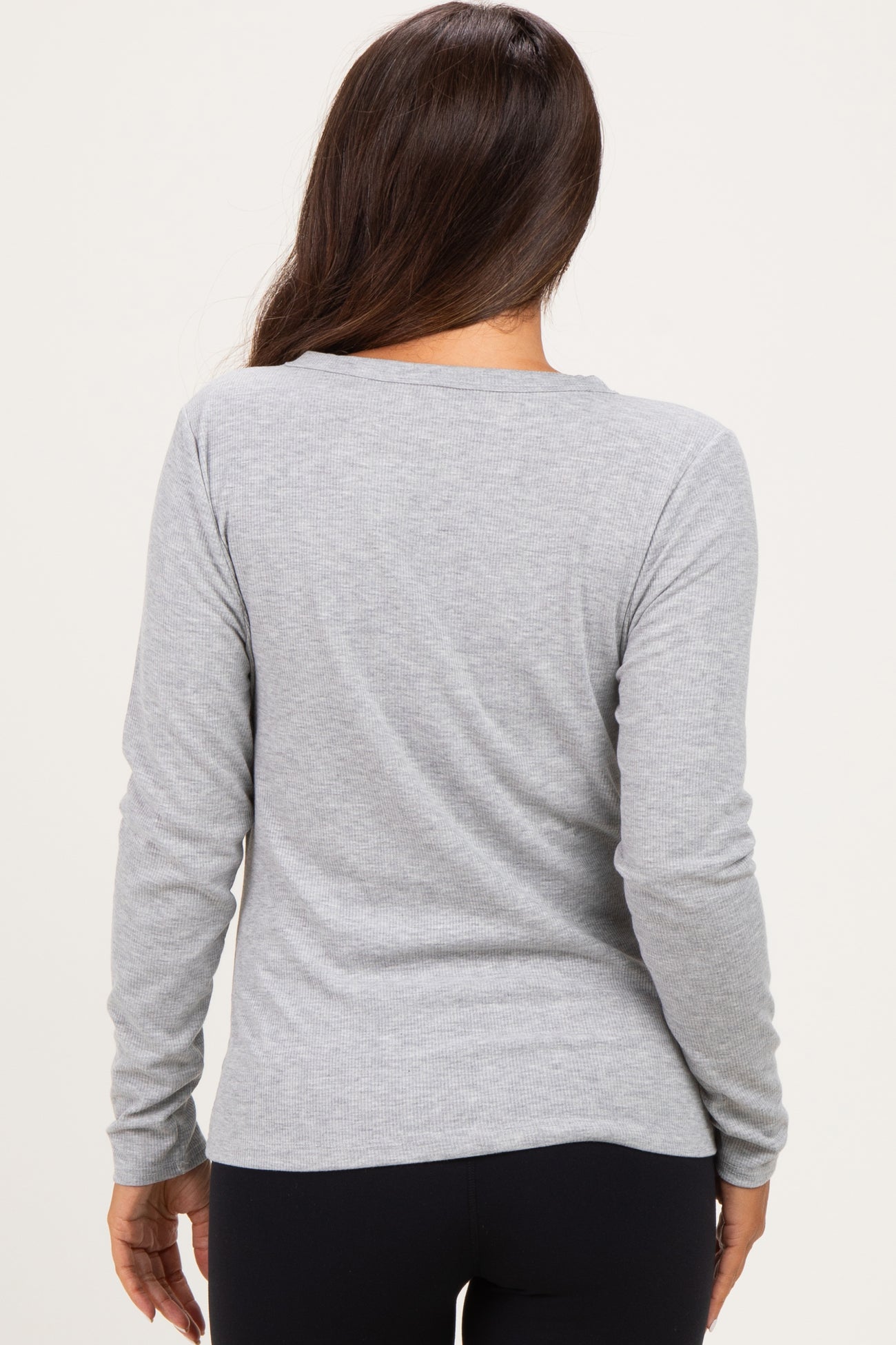 woman wearing a light grey long sleeve maternity top, seen from the back, paired with black leggings