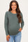 woman wearing a dark green long sleeve maternity top and smiling, showing her baby bump while styled with light blue jeans