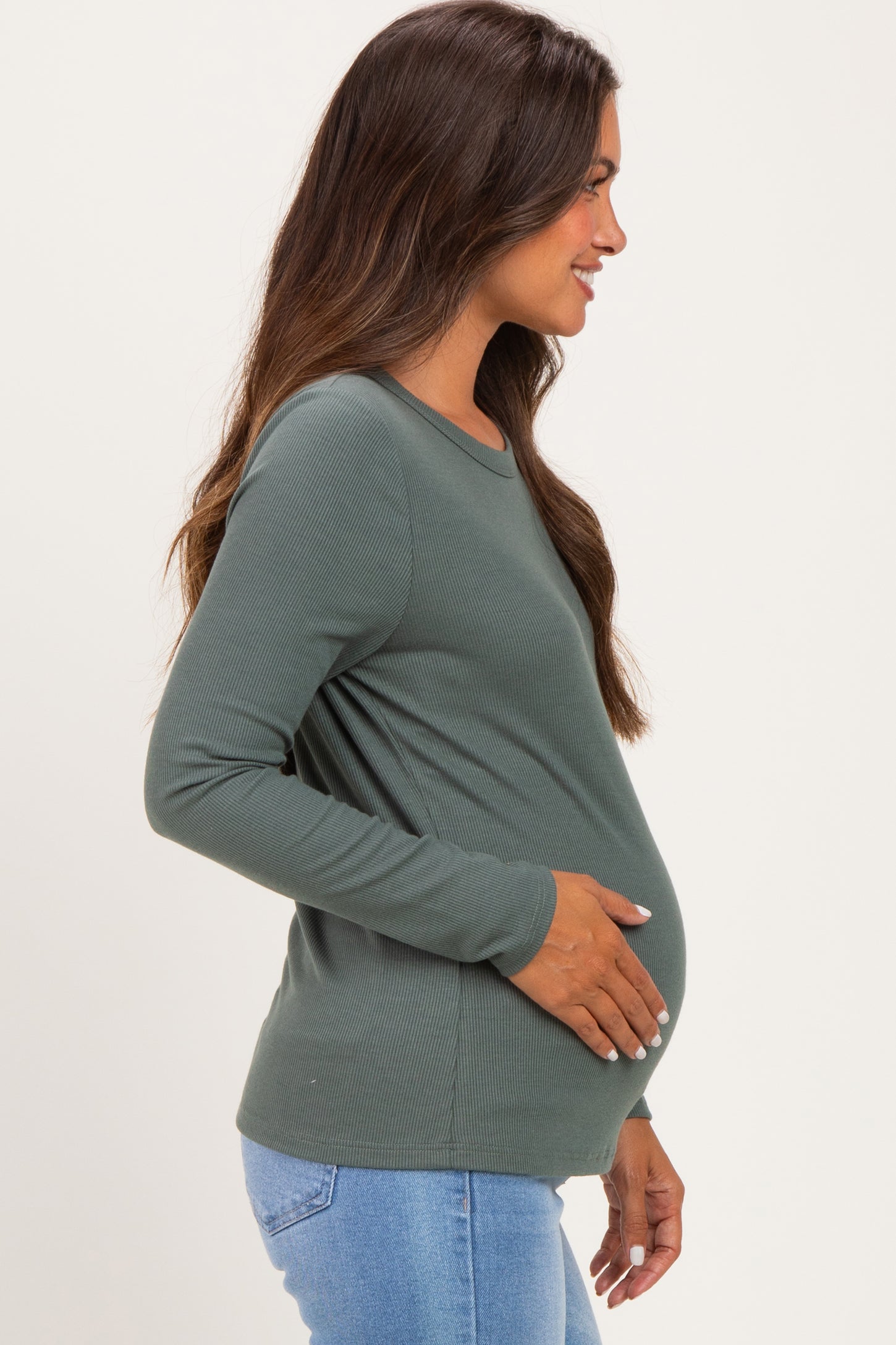 woman wearing a dark green long sleeve maternity top, gently holding her baby bump while smiling