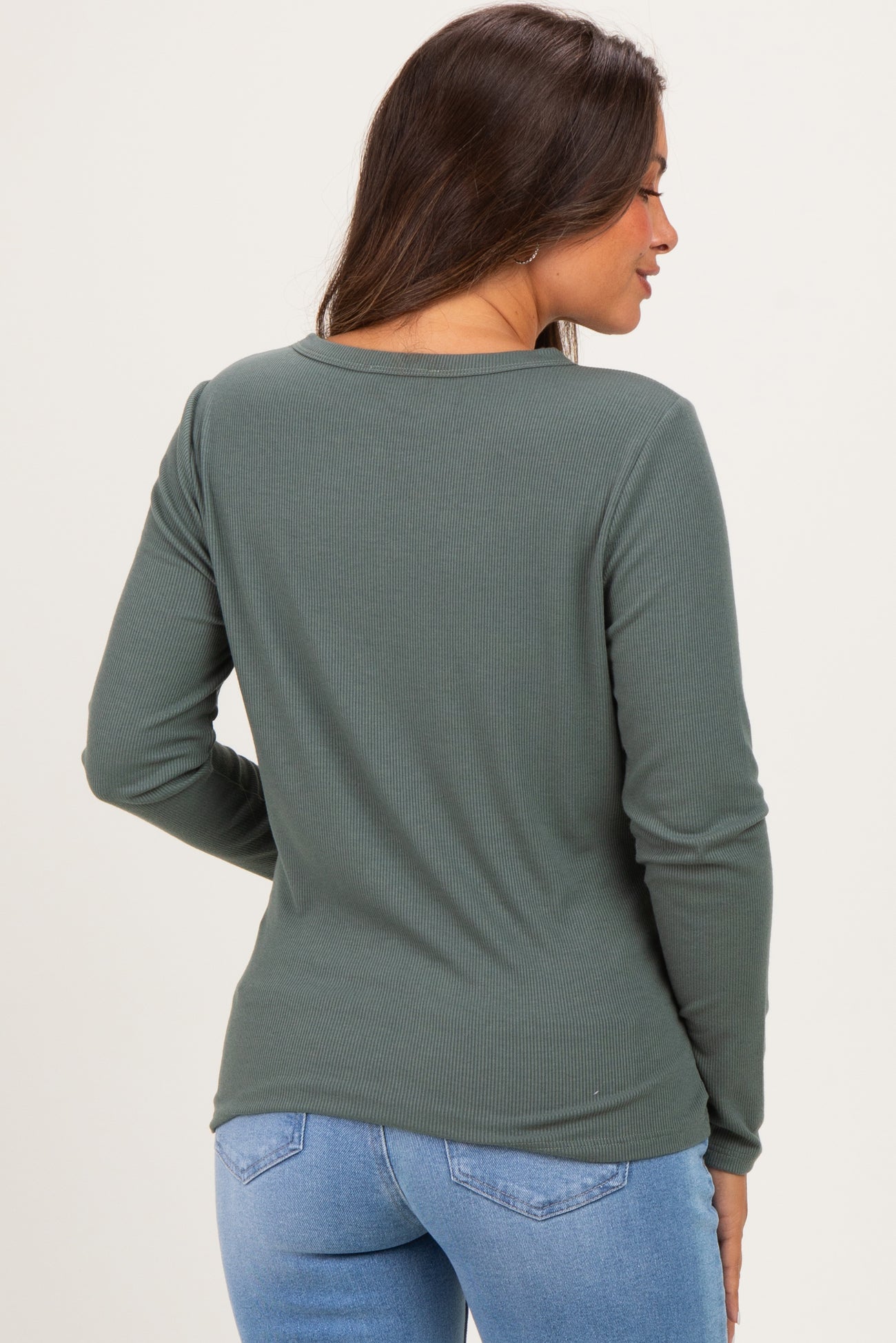 woman wearing a dark green long sleeve maternity top seen from the back paired with light blue jeans