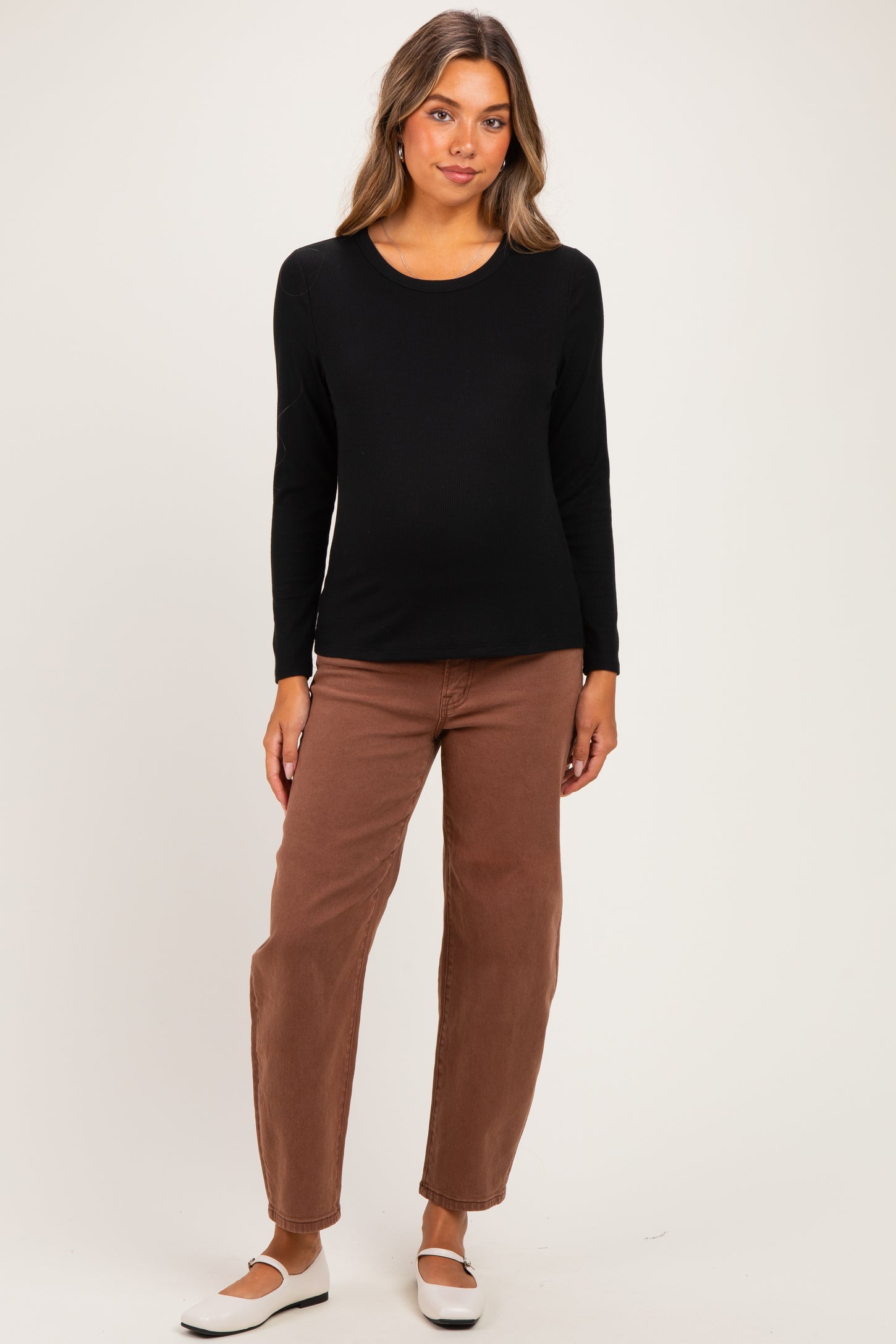 woman wearing a black long sleeve maternity top and brown pants with a visible baby bump