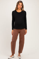 woman wearing a black long sleeve maternity top and brown pants with a visible baby bump