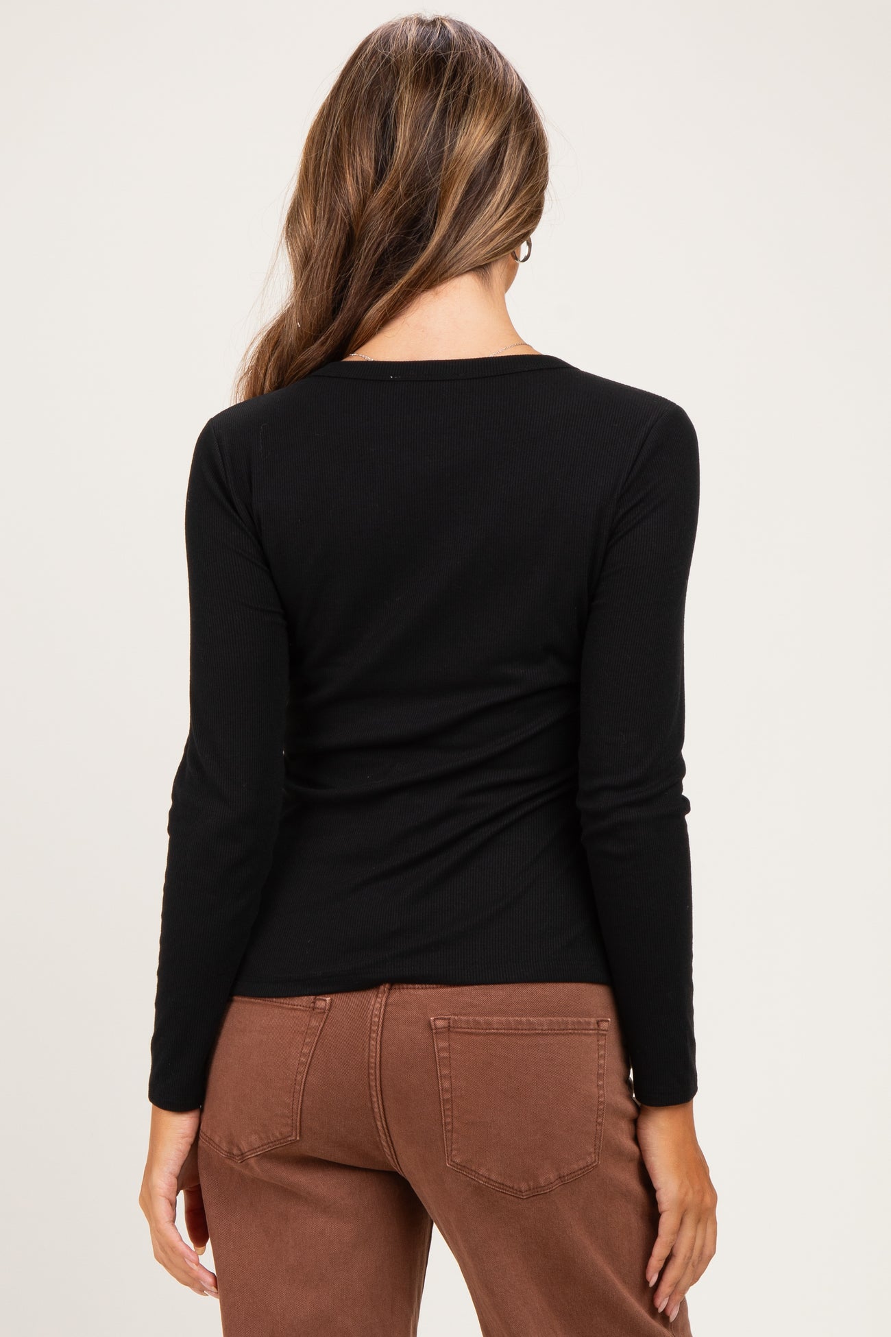 woman wearing a black long sleeve maternity top, visible baby bump, paired with brown pants from the back