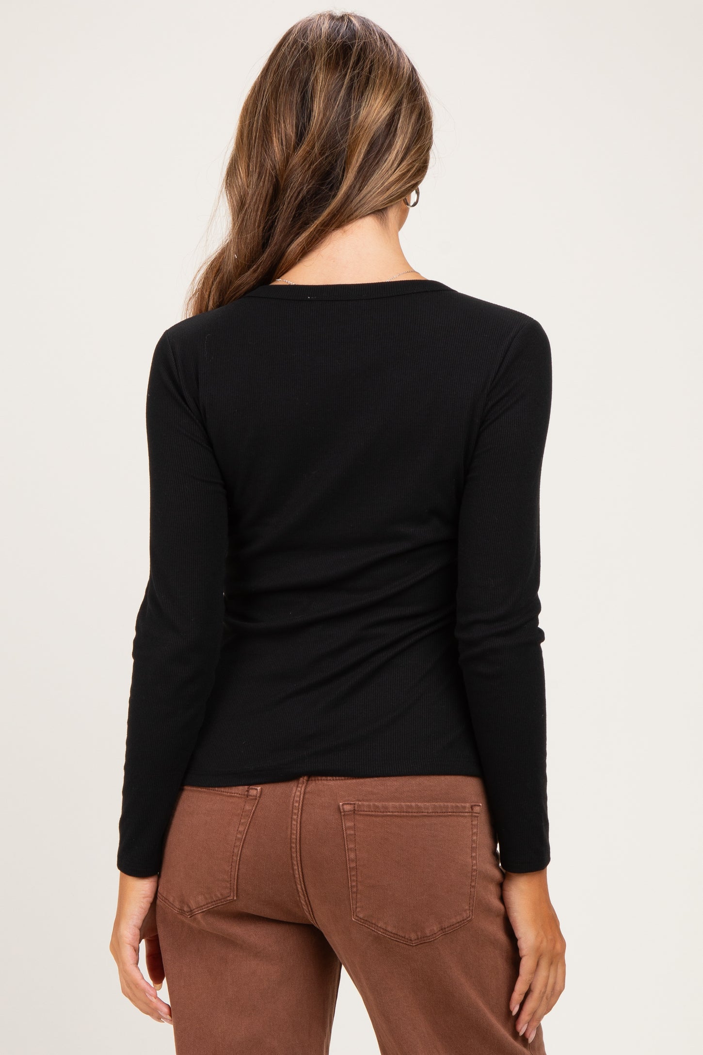 woman wearing a black long sleeve maternity top, visible baby bump, paired with brown pants from the back