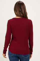woman wearing a burgundy long sleeve maternity top, viewed from the back, paired with blue jeans