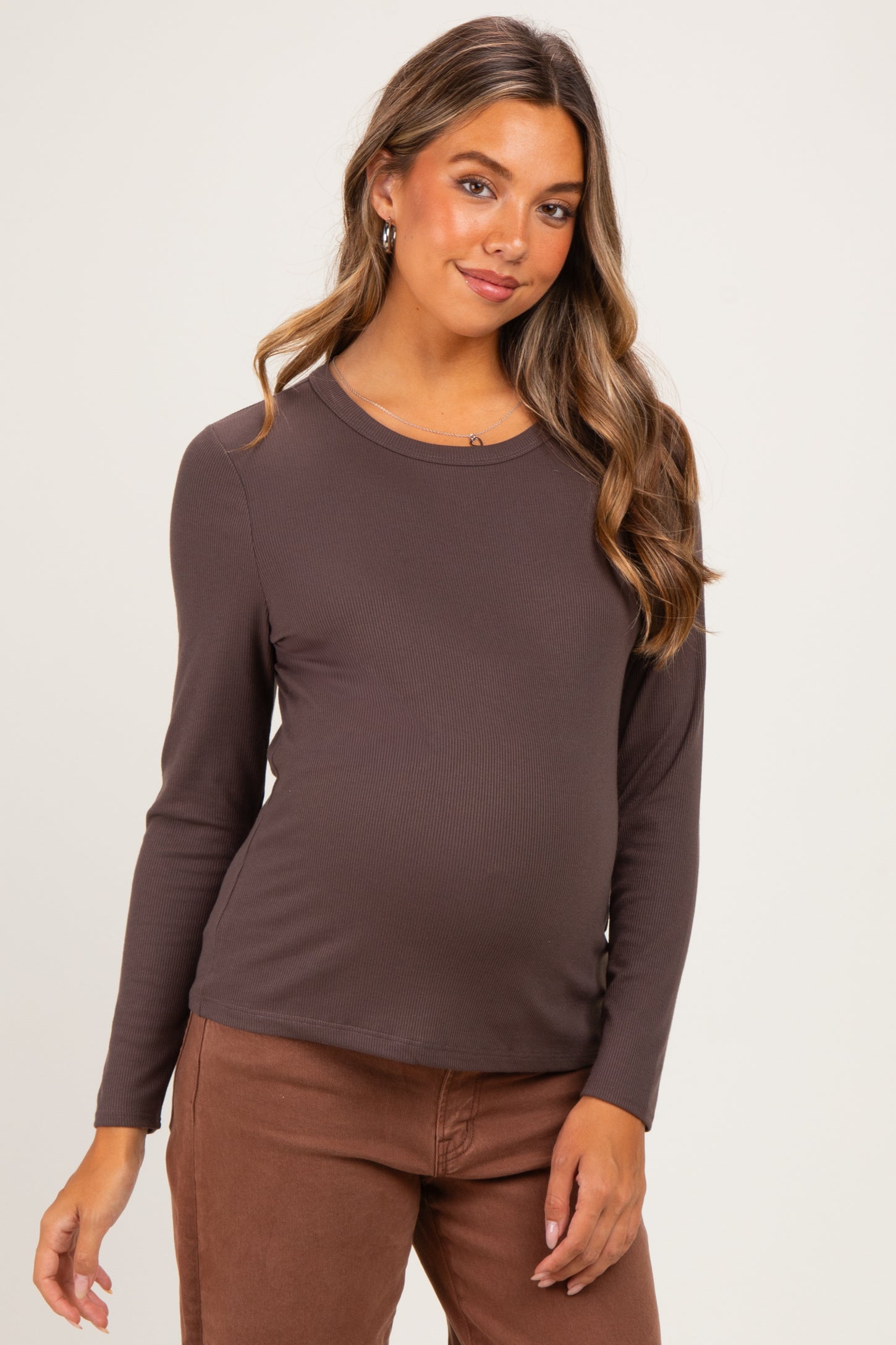 woman wearing a dark brown long sleeve maternity top and displaying her baby bump