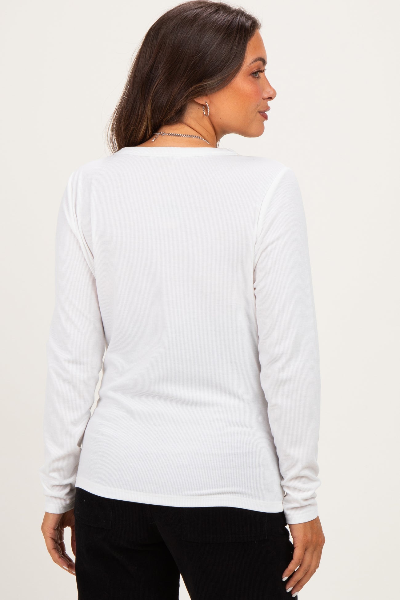 woman wearing a white long sleeve maternity top, seen from the back, with a fitted style and ribbed texture