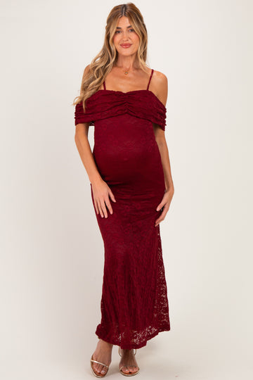 woman wearing a burgundy lace off-the-shoulder maternity dress with a fitted silhouette and a visible baby bump