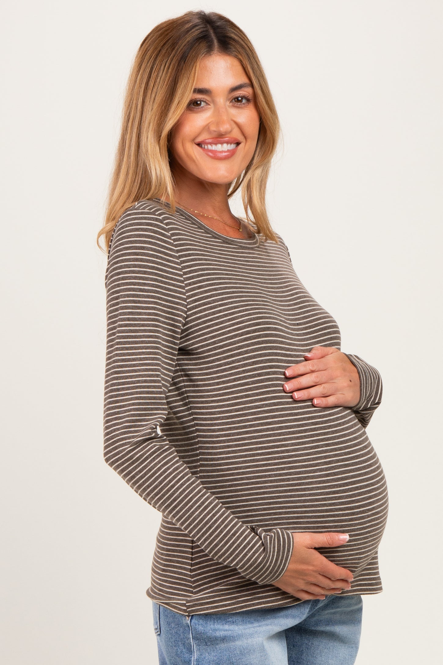 woman wearing a brown striped long sleeve maternity top and holding her baby bump