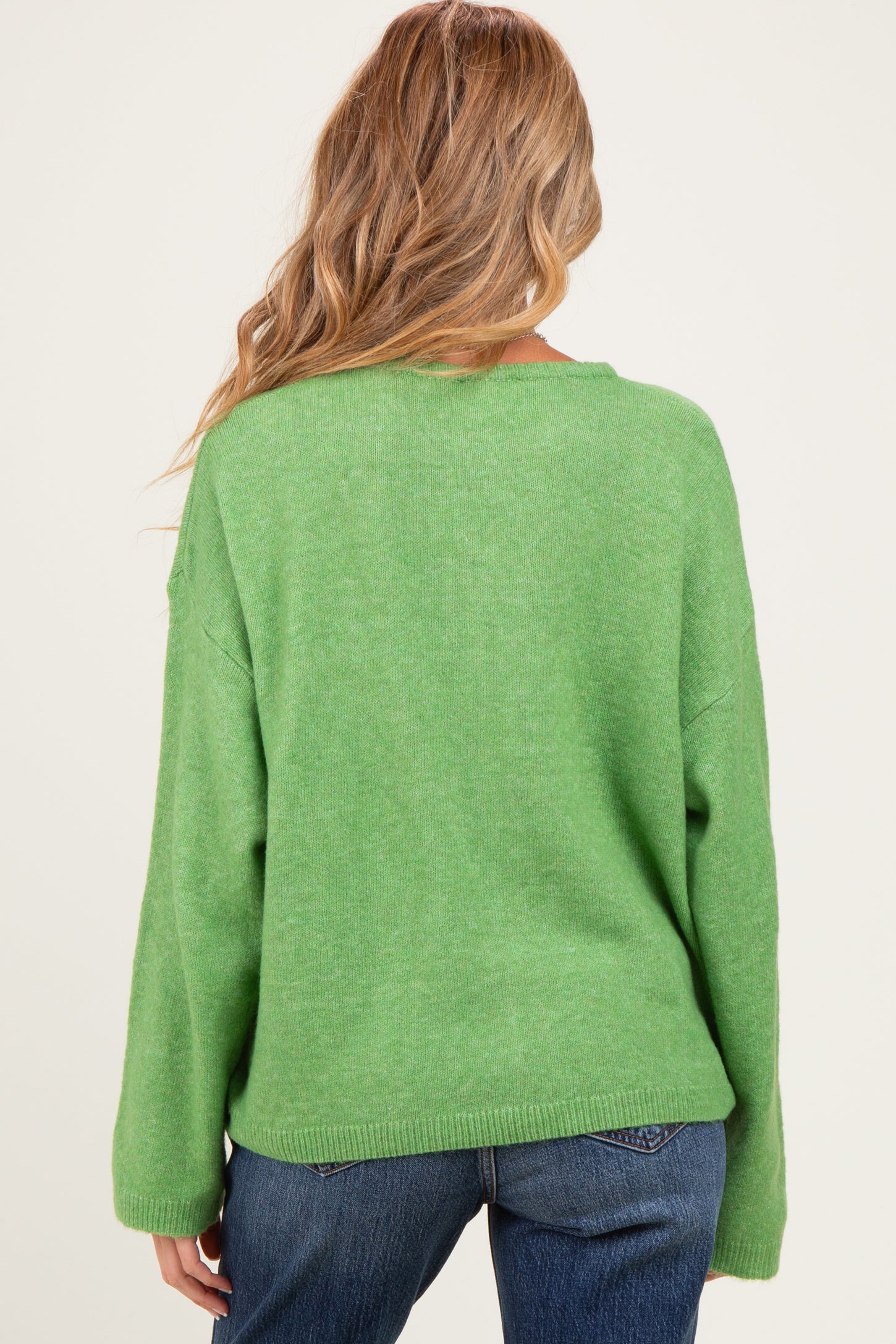 woman wearing a green oversized maternity sweater, viewed from the back, paired with blue jeans