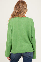 woman wearing a green oversized maternity sweater, viewed from the back, paired with blue jeans