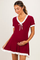 woman wearing a red ribbed maternity dress with white trim and a tie detail, gently cradling her baby bump