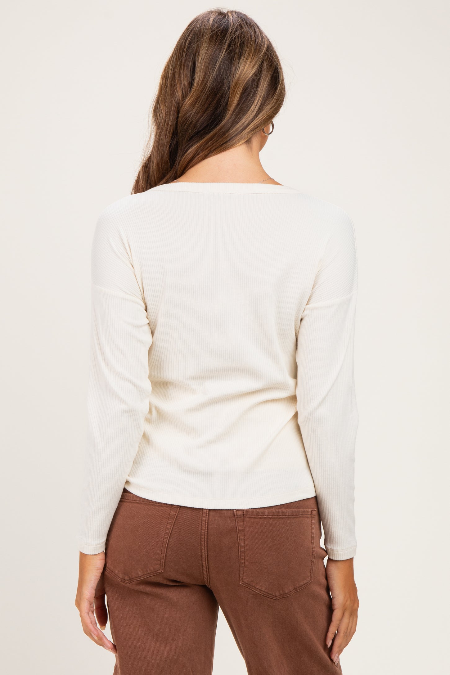 woman wearing a cream long sleeve maternity top, viewed from the back, paired with brown maternity pants
