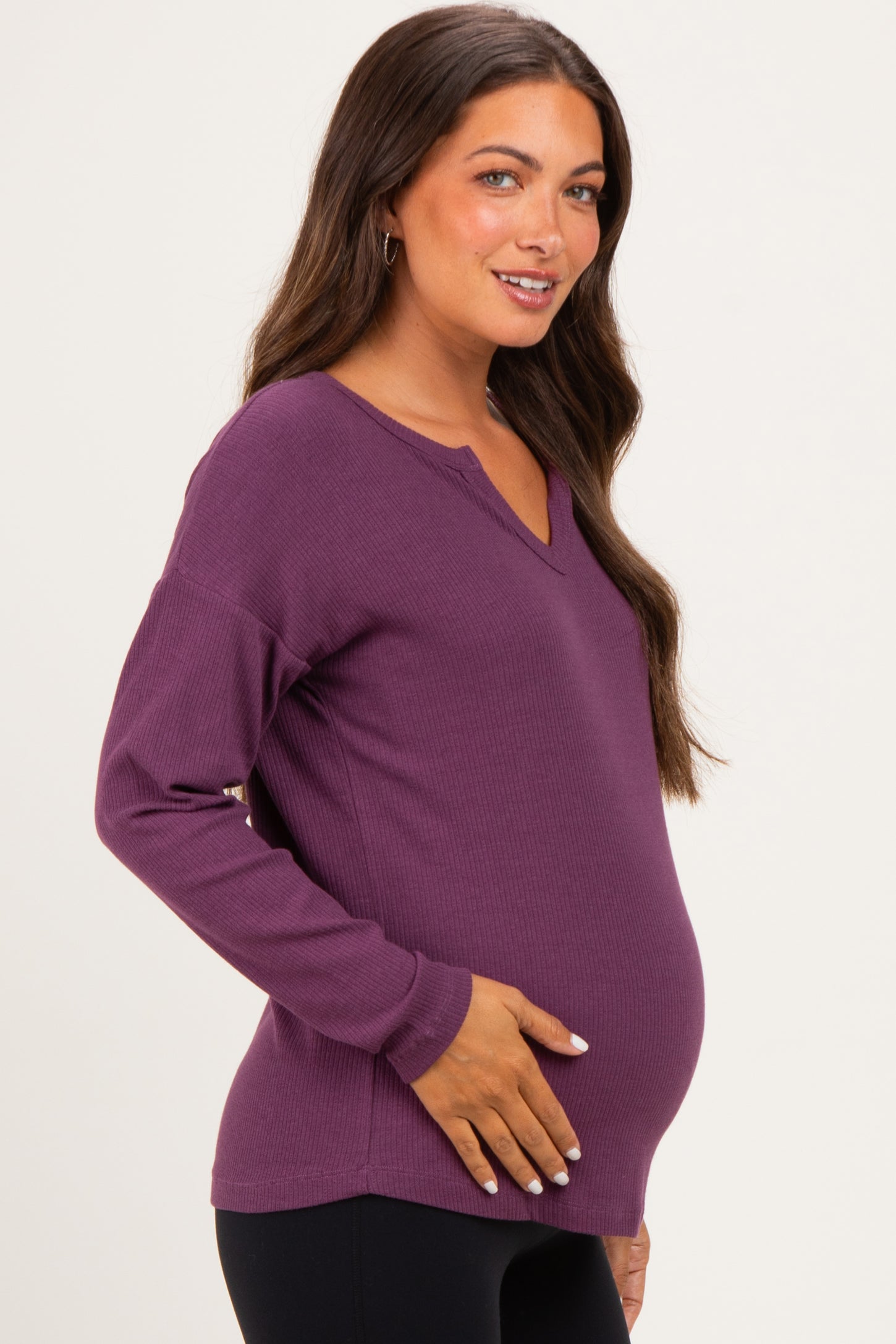 woman wearing a deep purple long sleeve maternity top and holding her baby bump