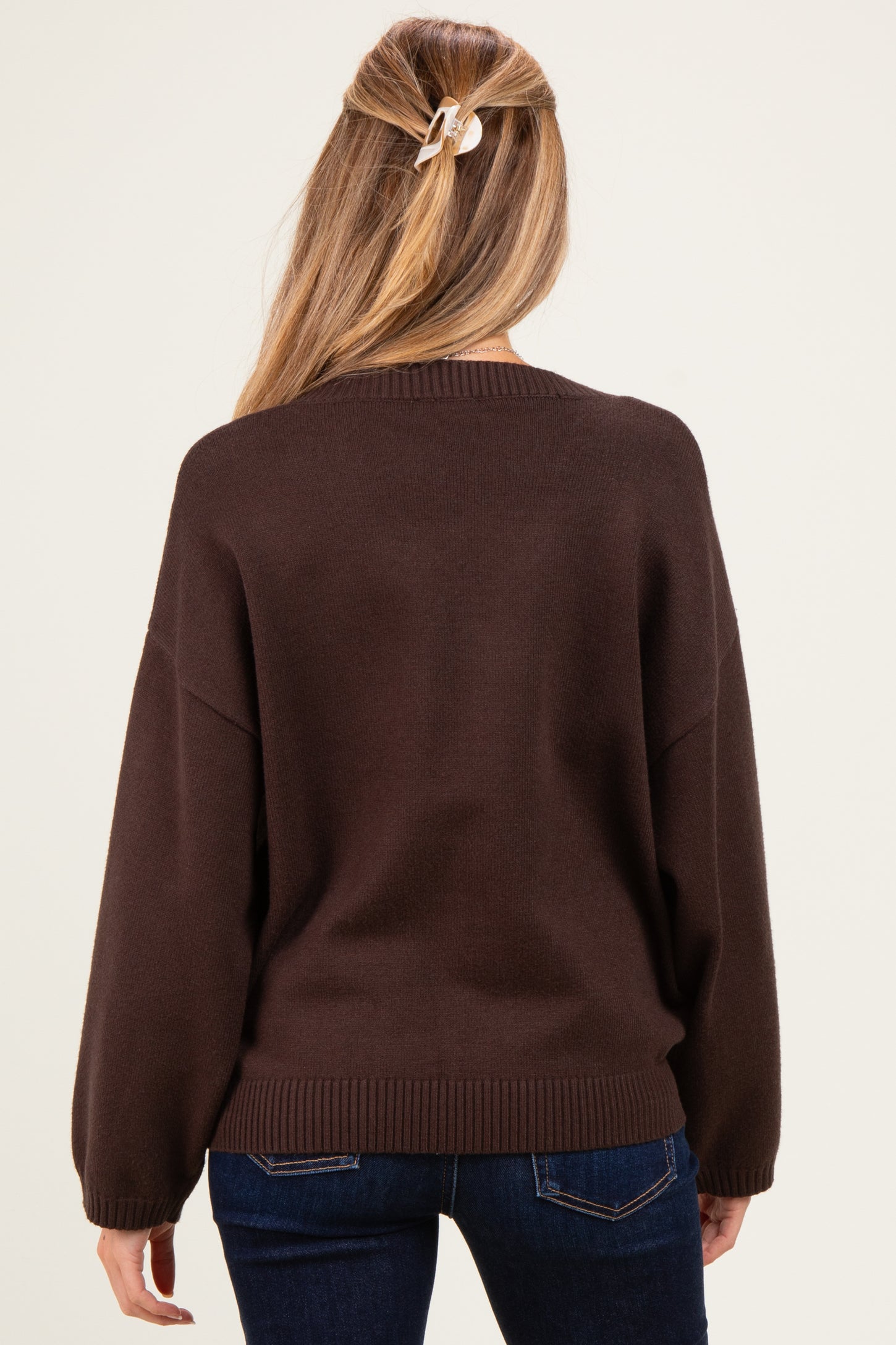 woman wearing a dark brown oversized maternity sweater, view from the back, styled with jeans and a hair clip