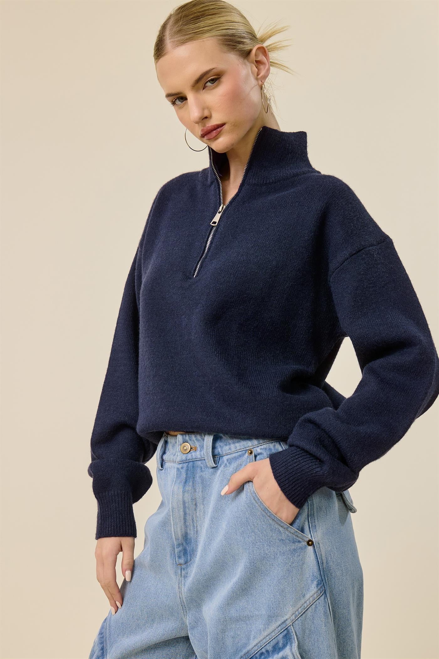 woman wearing a navy blue zip-up sweater with a high collar and relaxed fit, paired with light blue baggy jeans