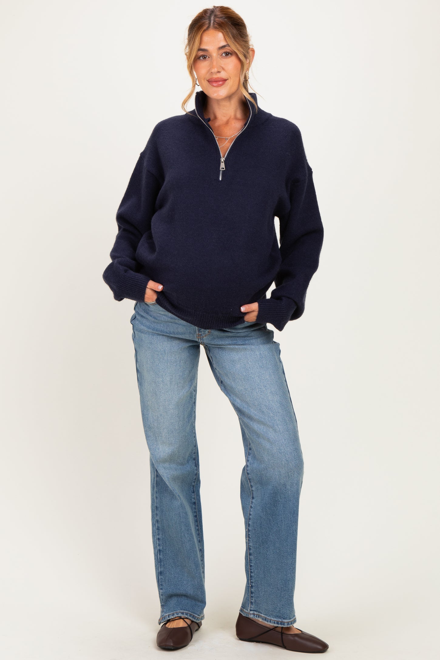 woman wearing a navy blue maternity zip-up sweater and flared jeans, with a visible baby bump