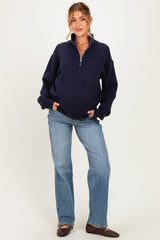 woman wearing a navy blue maternity zip-up sweater and flared jeans, with a visible baby bump