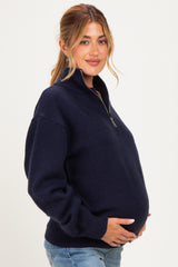 woman wearing a navy blue zip-up maternity sweater and holding her baby bump