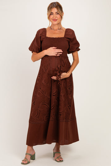woman wearing a brown maternity dress with puff sleeves and embroidery, holding her baby bump