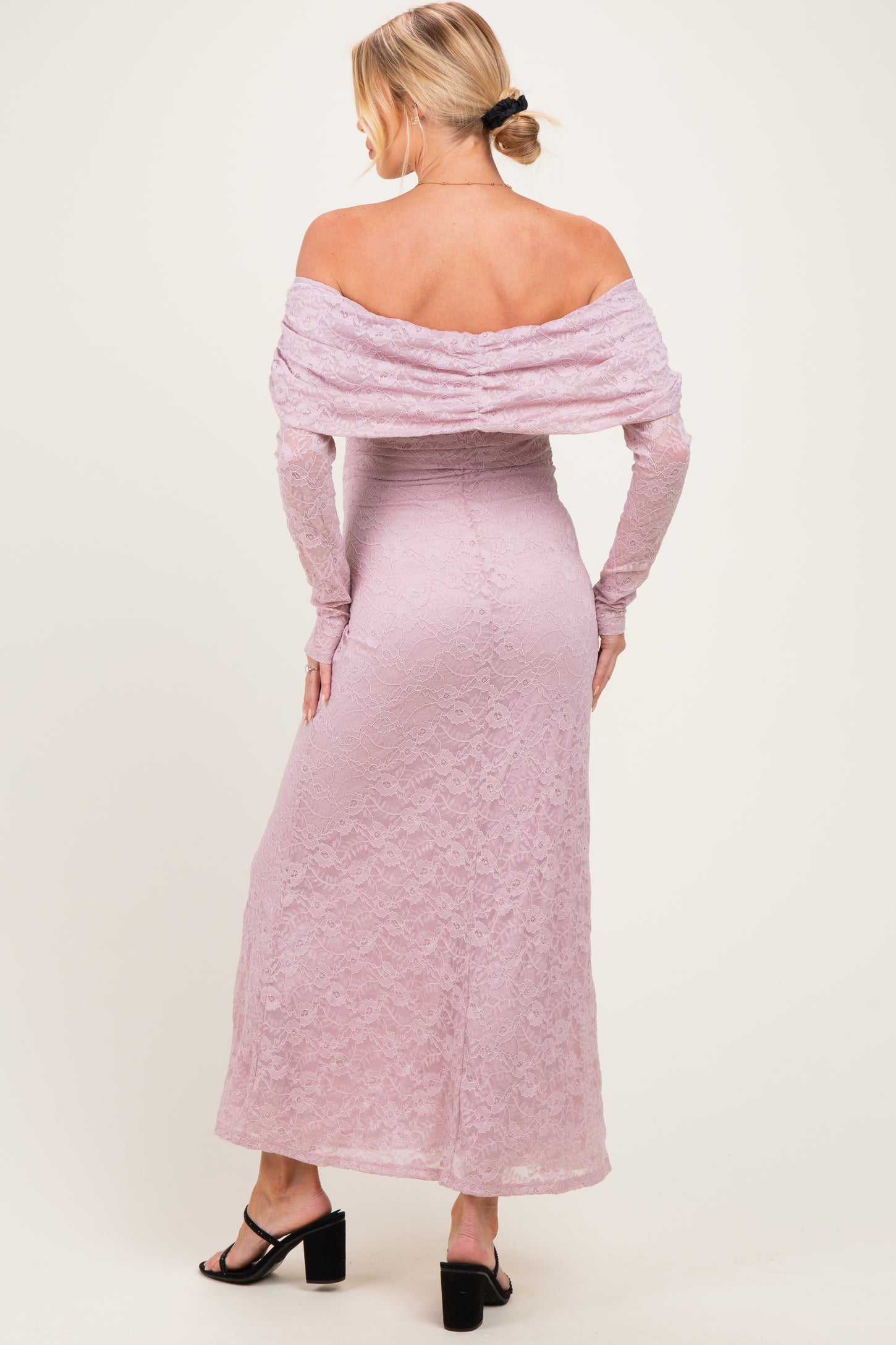 woman wearing a blush pink off-shoulder lace maternity dress with long sleeves and a fitted silhouette