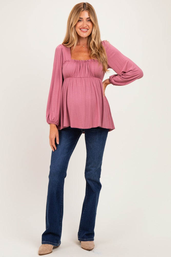 woman wearing a mauve long sleeve maternity top with a smocked bodice and a baby bump, paired with blue jeans