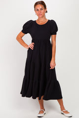 woman wearing a black puff sleeve midi dress with tiered ruffles and a round neckline