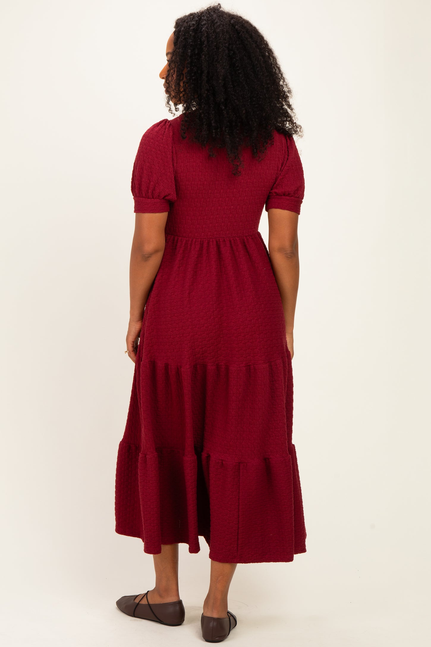 woman wearing a burgundy tiered maxi dress with short puff sleeves and a textured fabric