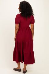woman wearing a burgundy tiered maxi dress with short puff sleeves and a textured fabric