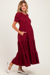 woman wearing a burgundy maternity maxi dress with puff sleeves and side pockets, showing her baby bump