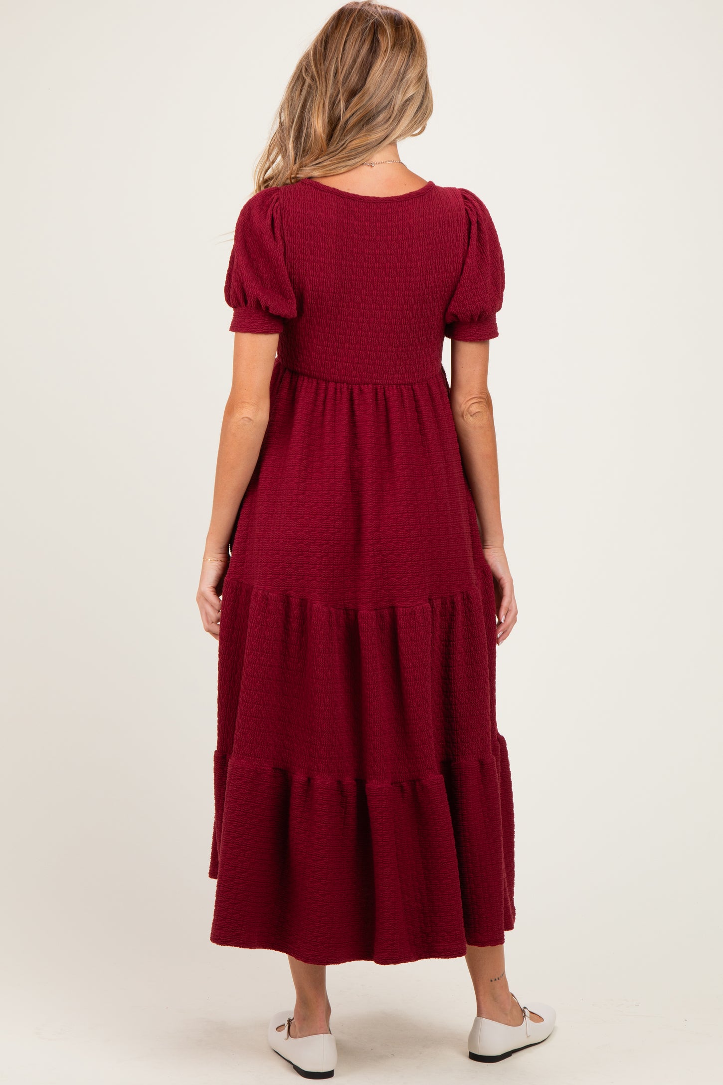 woman wearing a burgundy maternity maxi dress with puff sleeves and tiered skirt, showing a baby bump from the back