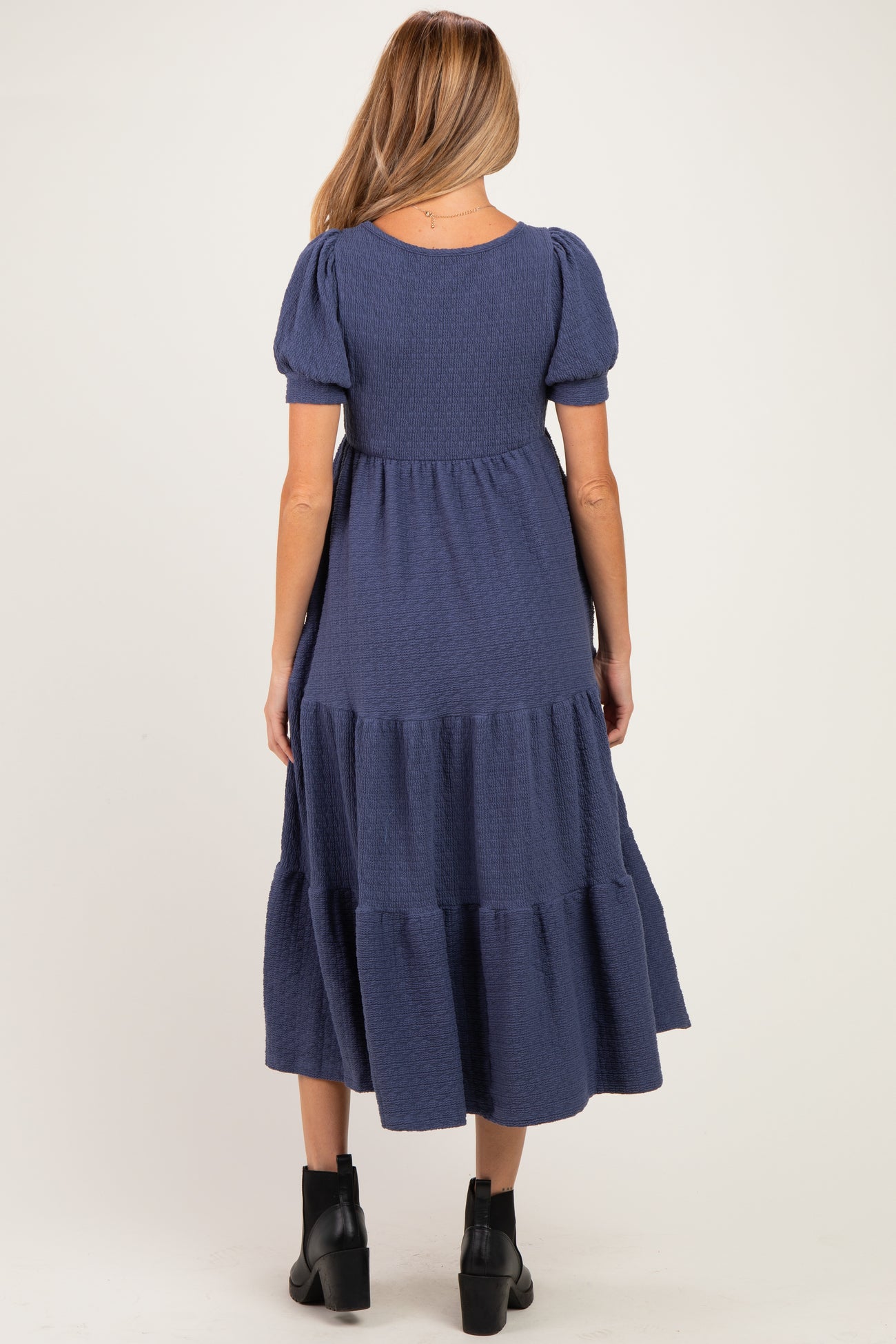 woman wearing a navy blue tiered maternity dress with short puff sleeves, showing the back view