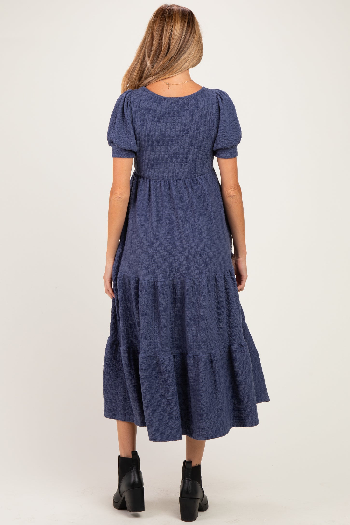 woman wearing a navy blue tiered maternity dress with short puff sleeves, showing the back view