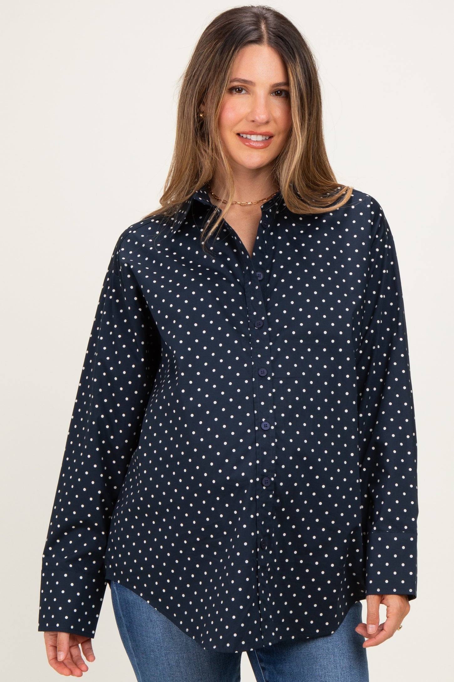 woman wearing a navy maternity button-up shirt with white polka dots and a visible baby bump
