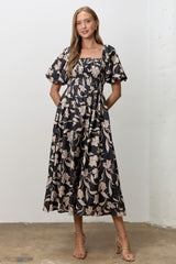 woman wearing a black floral midi dress with puff sleeves and a smocked bodice, standing with hands in pockets