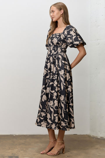 woman wearing a black floral print midi dress with puff sleeves and a fitted bodice, standing sideways