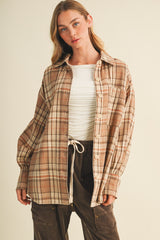 woman wearing a brown plaid oversized shirt over a white fitted top, styled with dark brown pants