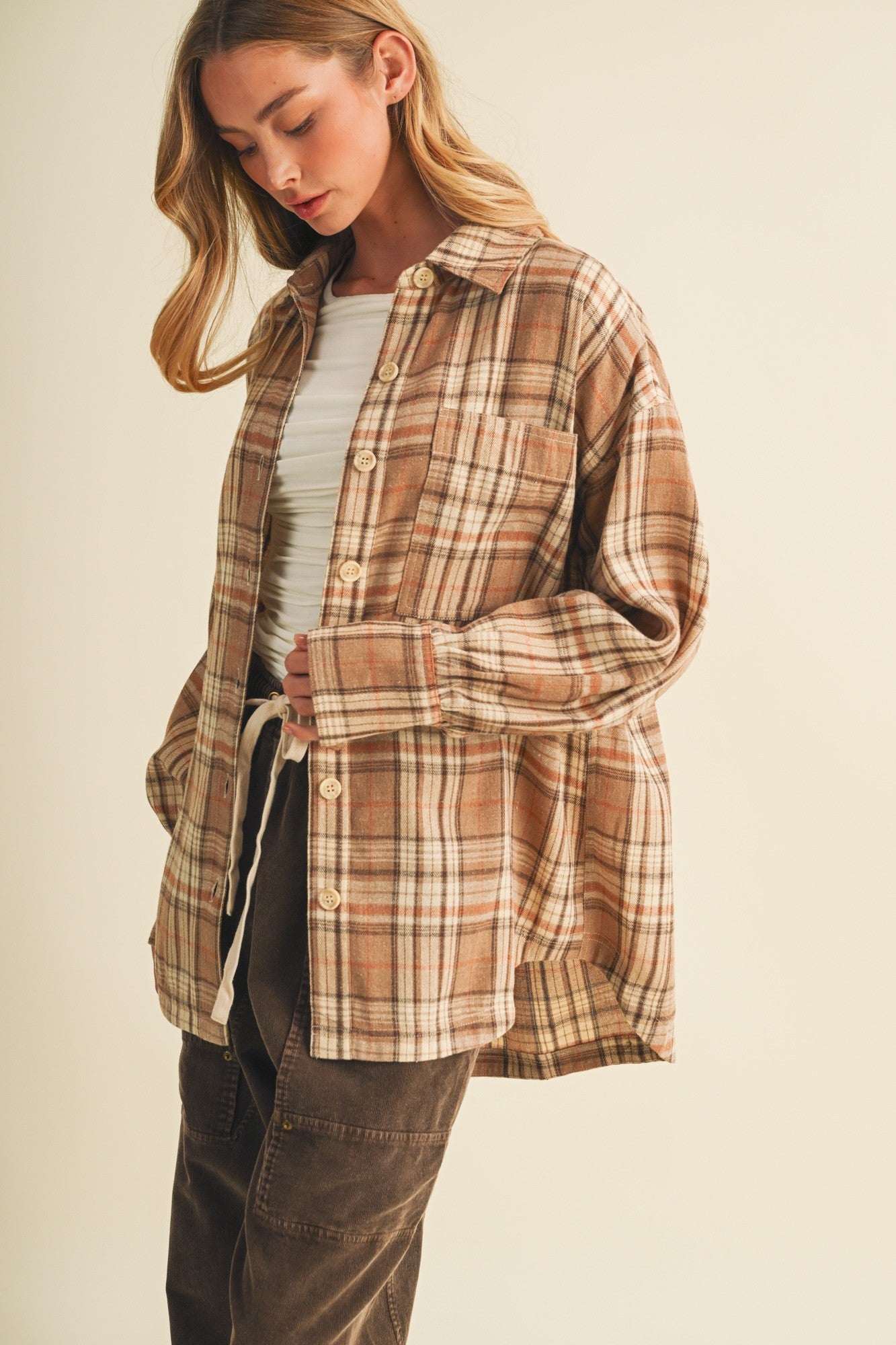woman wearing a brown plaid oversized button-up shirt and a white top, styled with loose brown pants