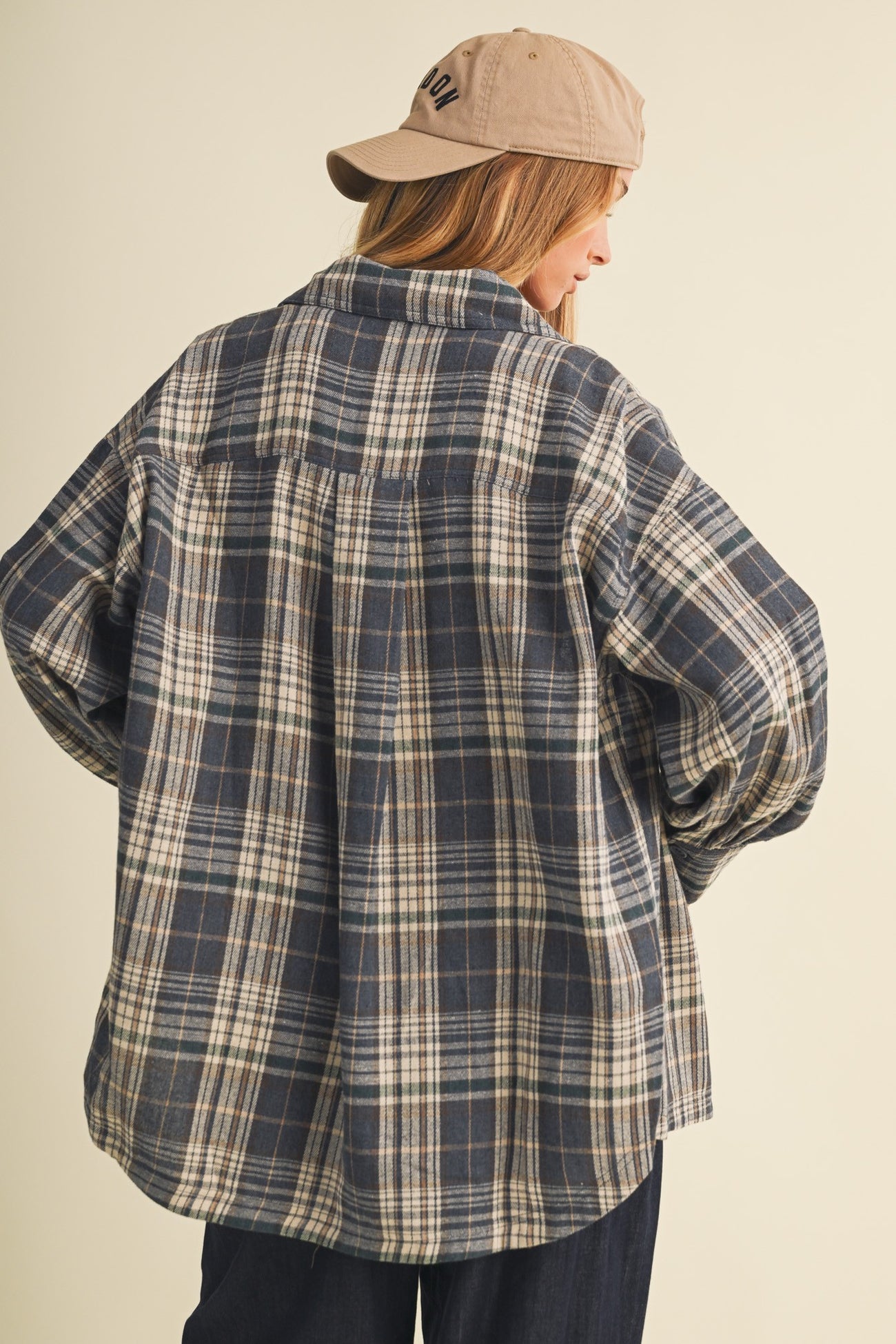 woman wearing a navy plaid oversized flannel shirt with a back view and a beige baseball cap