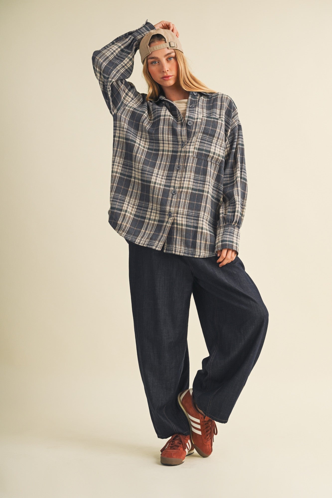 woman wearing an oversized navy plaid shirt and wide-leg denim pants, styled with a cap and red sneakers