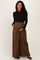 woman wearing a black long sleeve top and brown wide-leg maternity pants, holding her baby bump.