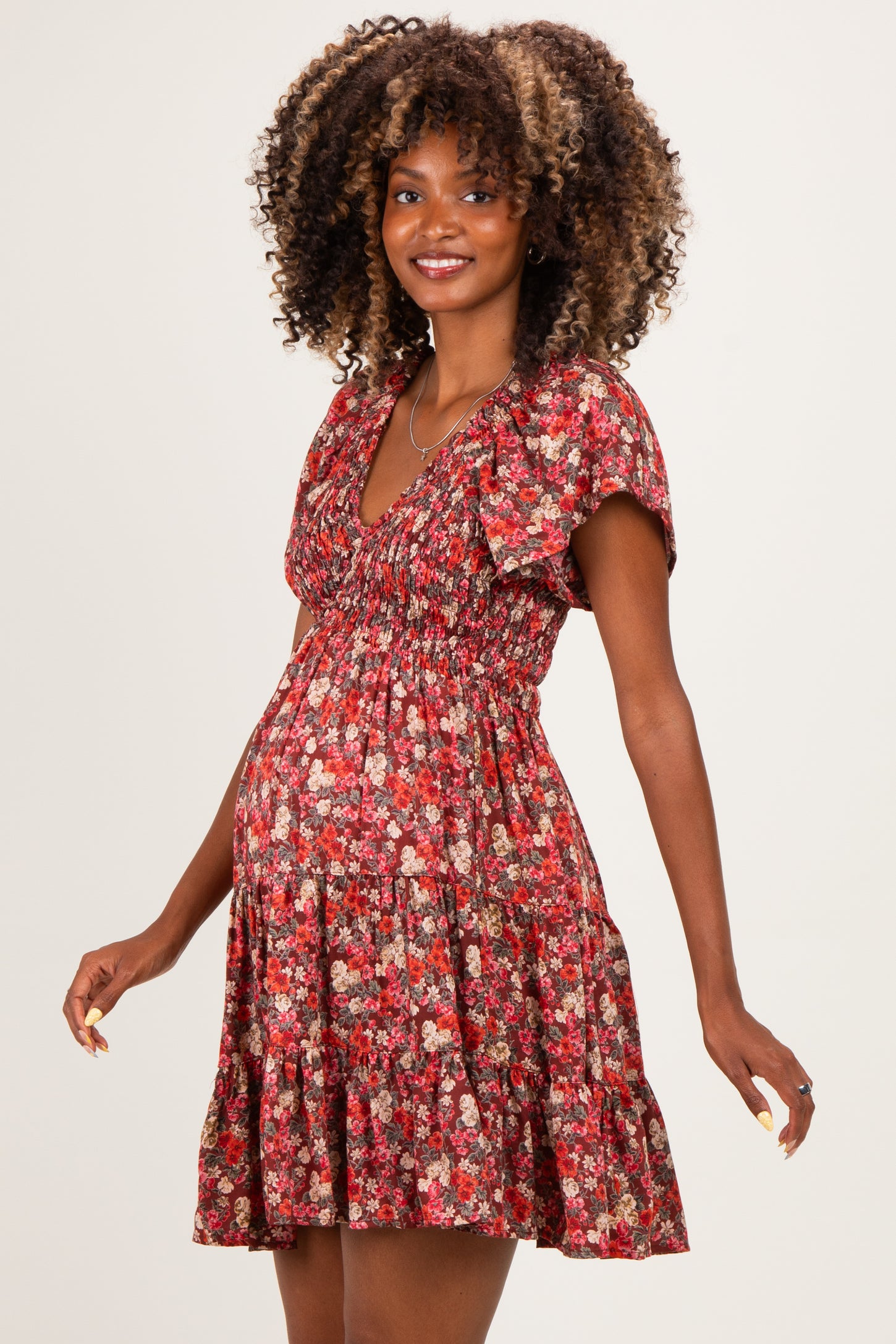 woman wearing a red floral maternity dress with a smocked bodice and flutter sleeves, showcasing her baby bump