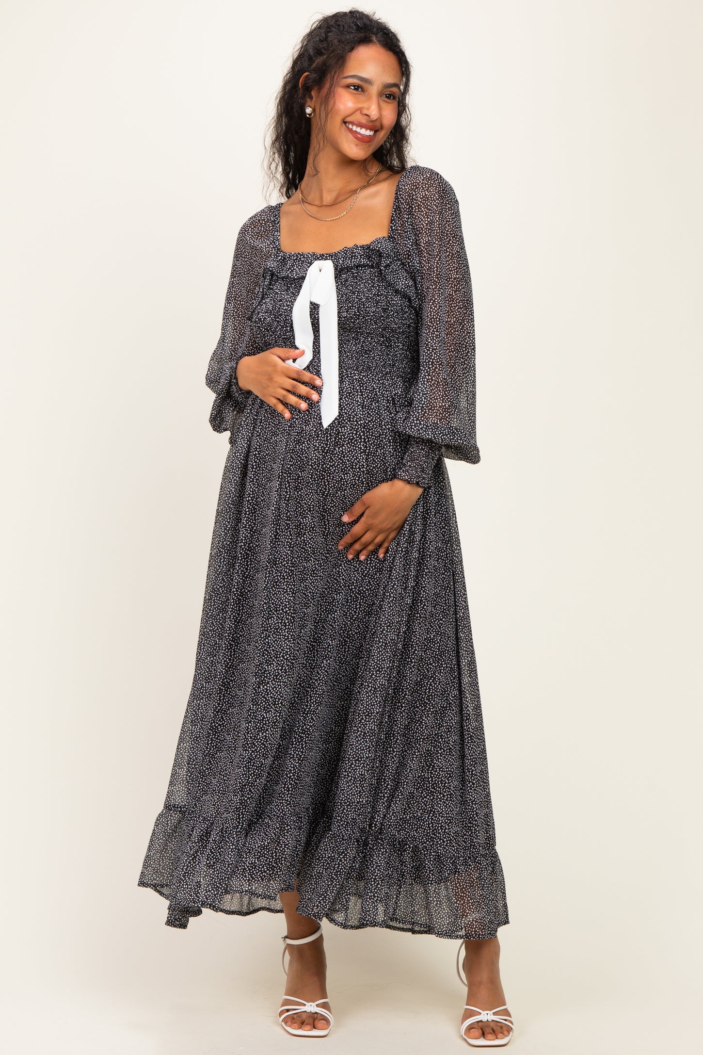 woman wearing a black and white patterned maternity dress with long sleeves and a tie at the neckline, showing her baby bump
