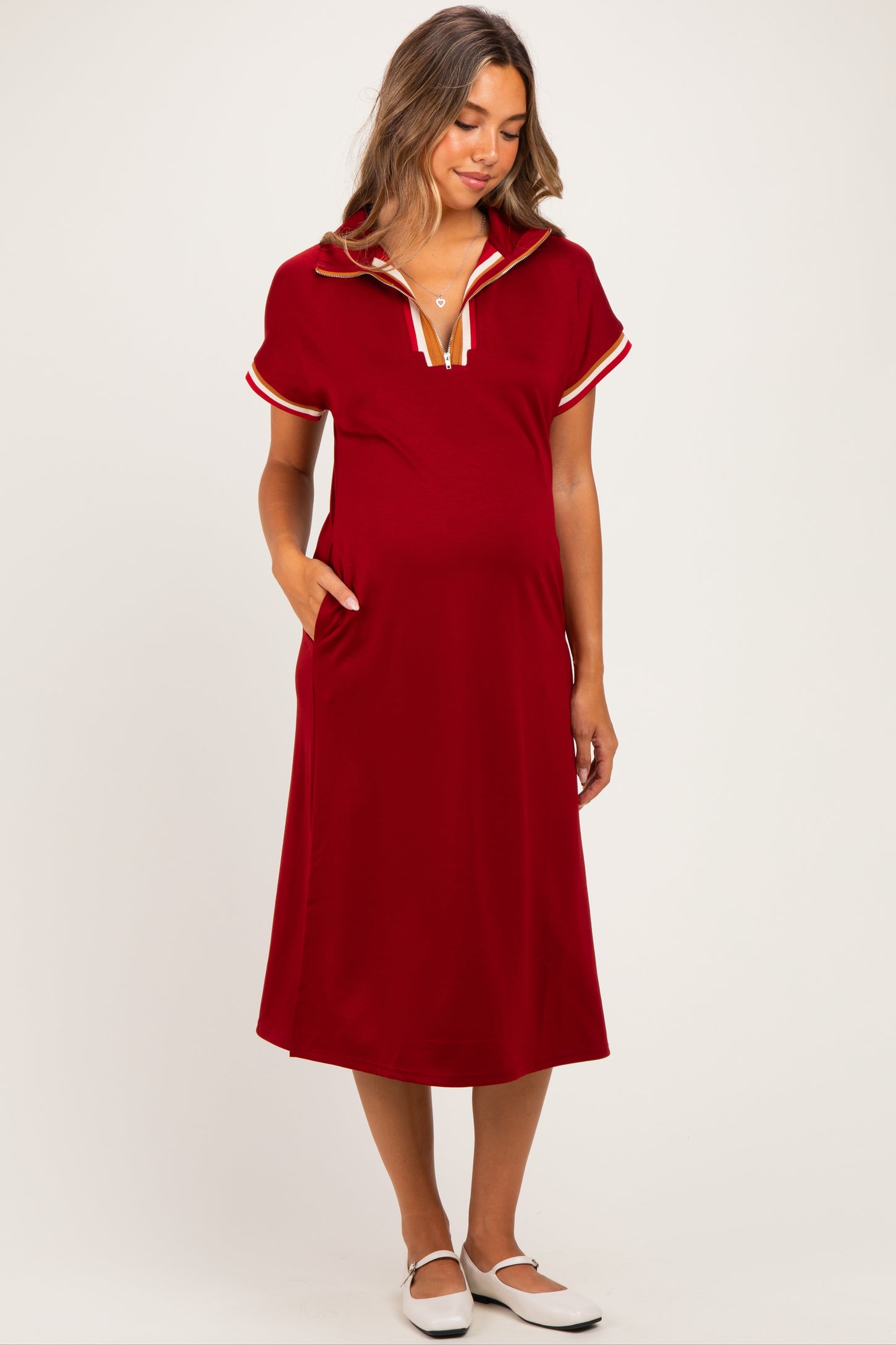 woman wearing a red maternity dress with a collar and short sleeves, featuring a sporty design and side pockets, with a visible baby bump