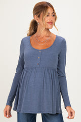 woman wearing a blue ribbed long sleeve maternity top with button detail and a flared silhouette, showcasing her baby bump