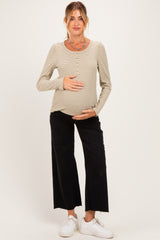 woman wearing a beige striped maternity top with button details and black wide-leg maternity pants, holding her baby bump