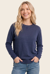 woman wearing a navy blue long sleeve sweater with a crew neckline and side slits, smiling and hands in pockets